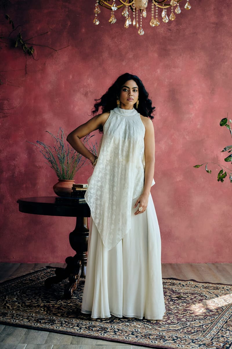 A woman in an ivory kaftan-style top worn over a flowing drape skirt